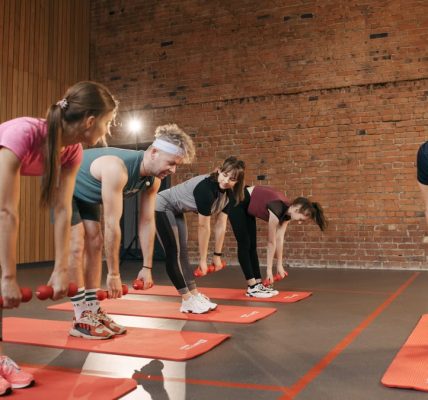 Fitness group performing exercises with dumbbells in a modern yoga studio setting.