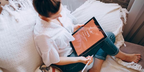 A woman relaxes on a sofa with a digital tablet, enjoying leisure time in a cozy home environment.